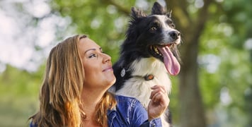 A woman looking up at her dog wearing an activity monitor.