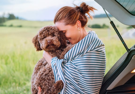 A woman in a striped blanket hugging her Maltipoo.