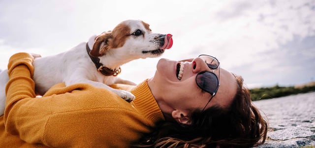 A happy woman with a white dog licking her face