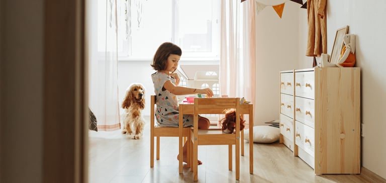 Child sitting drawing at a desk with Cocker Spaniel watching