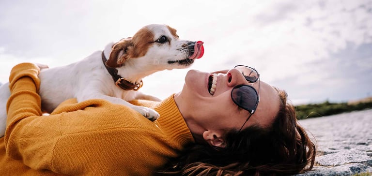 A happy woman with a white dog licking her face