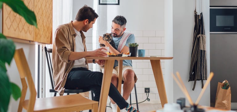 Two men sitting around a table with a cat.