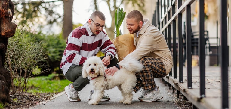 Two men crouching down with groceries and a dog.
