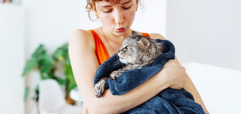 A woman holding a cat wrapped in a towel.