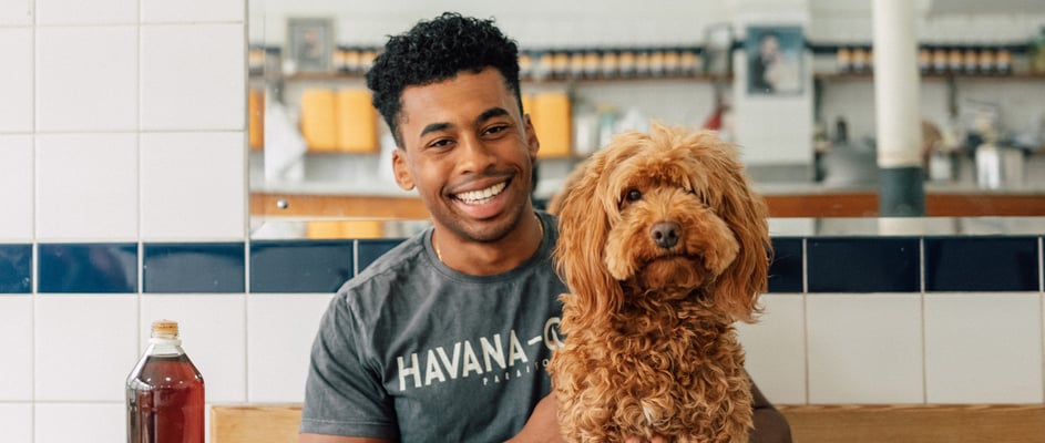 A man smiling in a cafe with his Cavapoo.