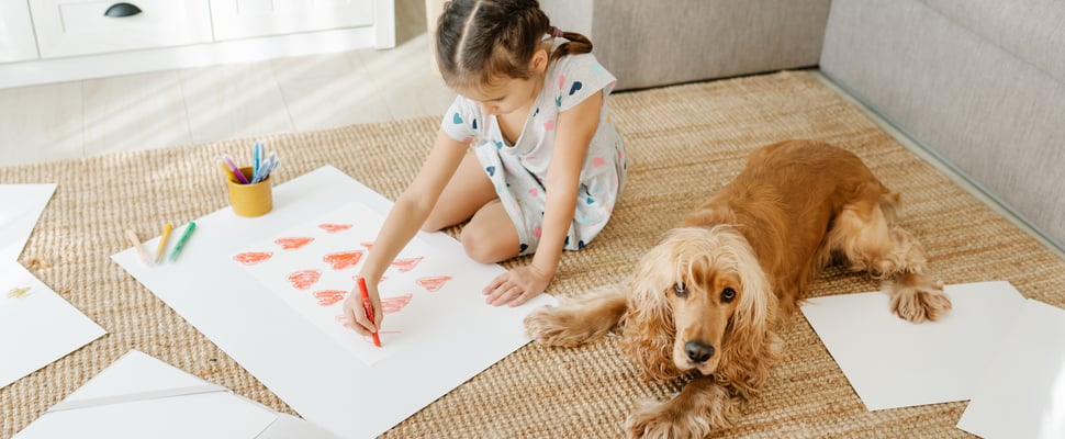 Child drawing hearts with Cocker Spaniel lying next to them